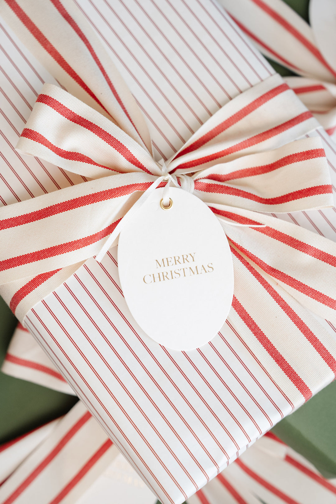 Oval gold foil Merry Christmas tag on a red pinstripe gift tied with red and cream striped ribbon