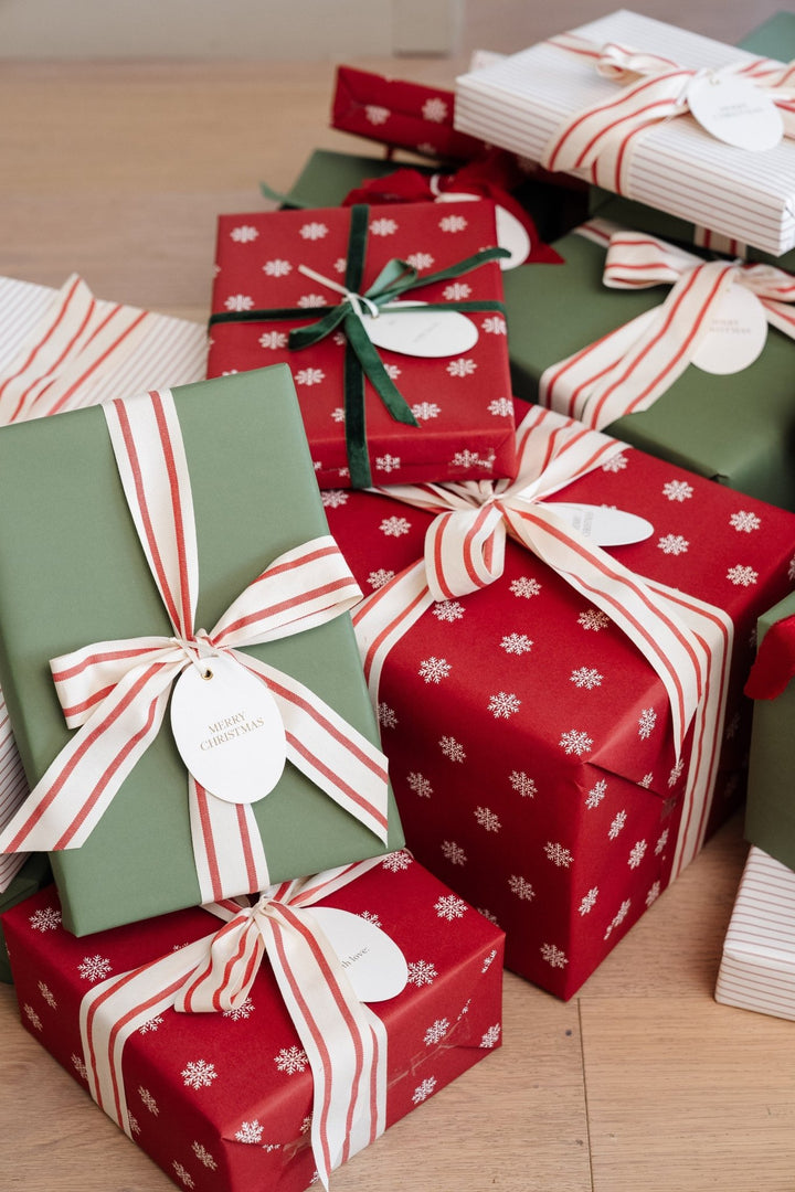 Stacked snowflake and green Christmas gifts on a pale wood floor with oval tags
