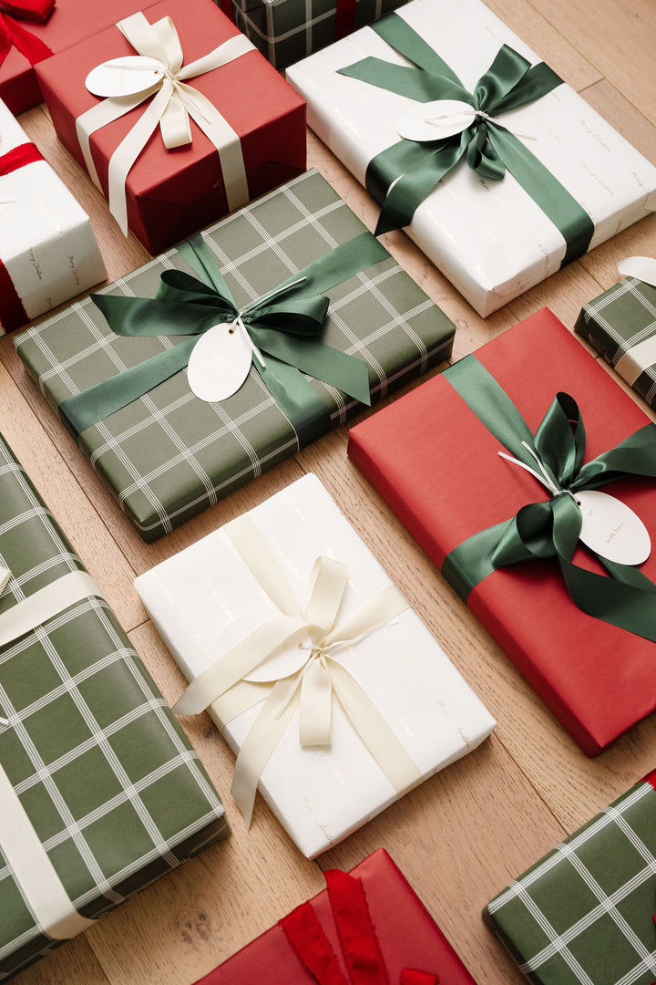 Overhead rows of plaid, red, and gold script gifts with green satin and cream grosgrain bows