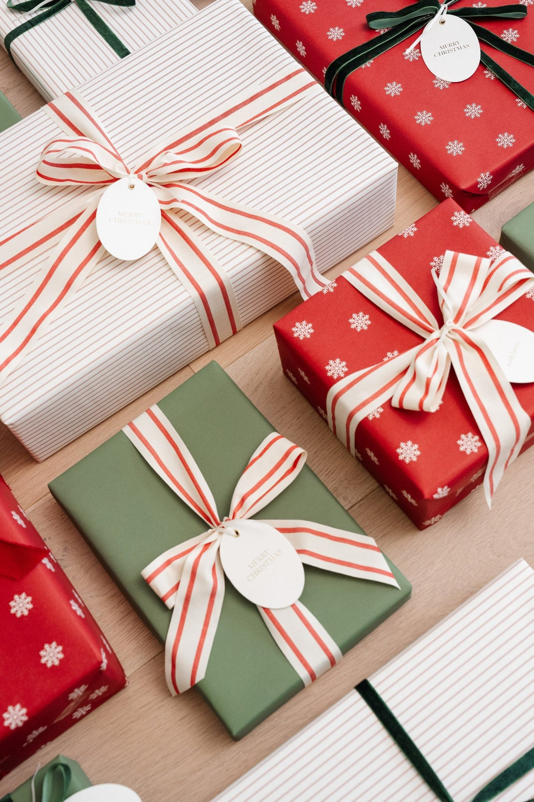 Overhead mix of red snowflake and green wrapped gifts with striped cotton bows and oval tags