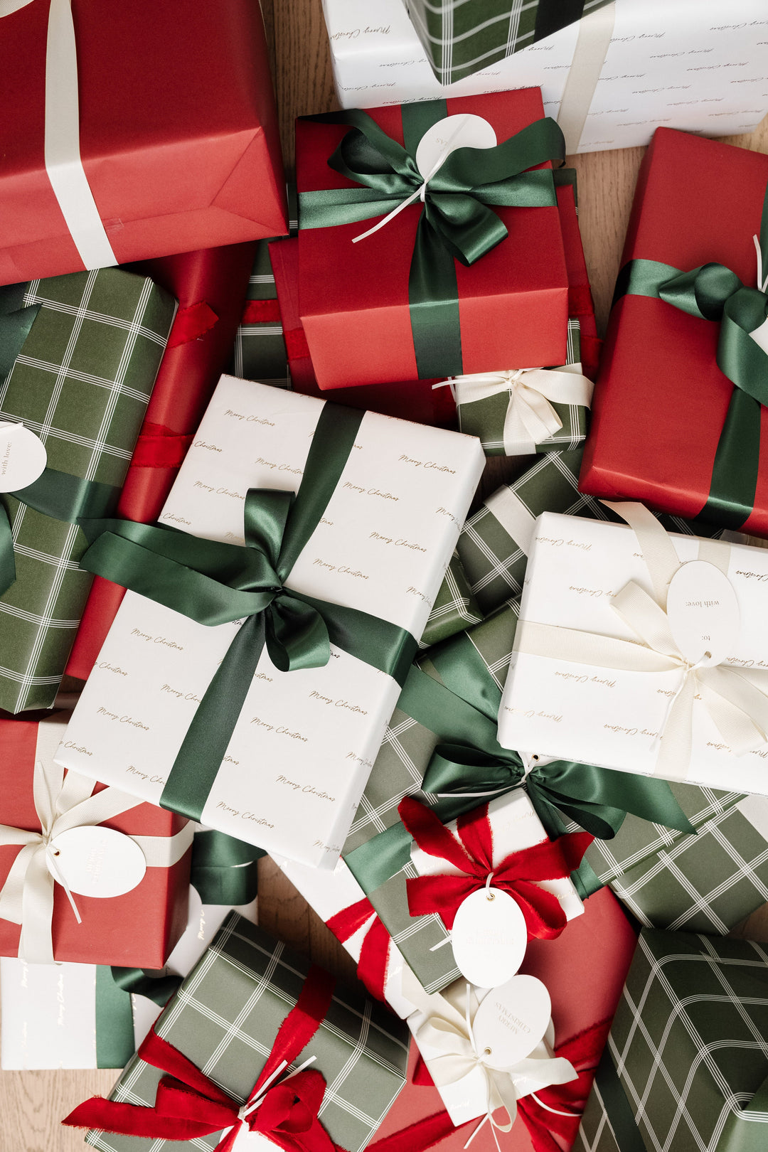 Pile of Christmas presents in gold Merry Christmas script, green plaid, and red paper with satin bows