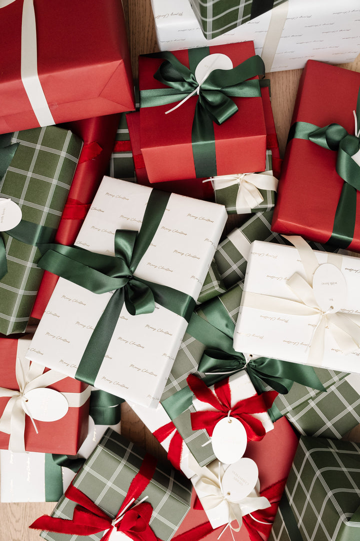 Pile of Christmas presents in gold Merry Christmas script, green plaid, and red paper with satin bows