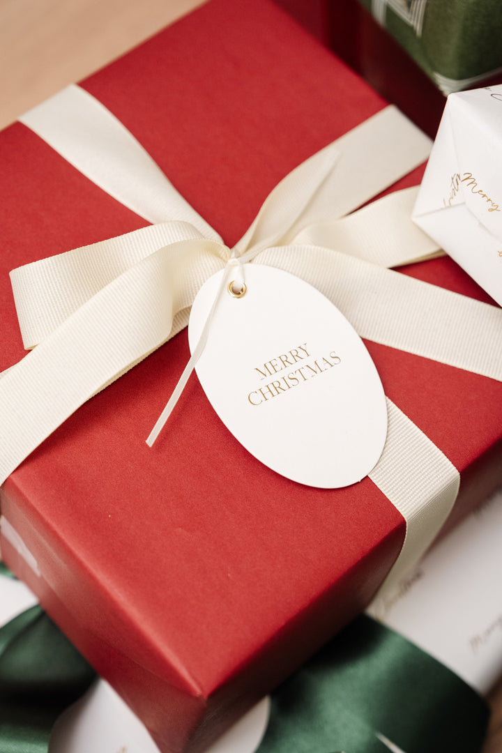 Oval Merry Christmas tag on a deep red gift with a cream grosgrain bow
