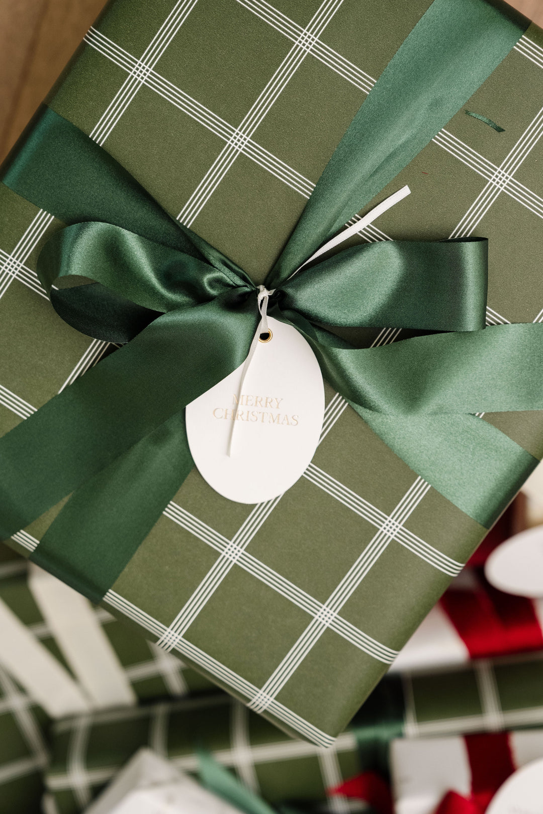Green windowpane plaid gift with a full green satin bow and an oval letterpress tag