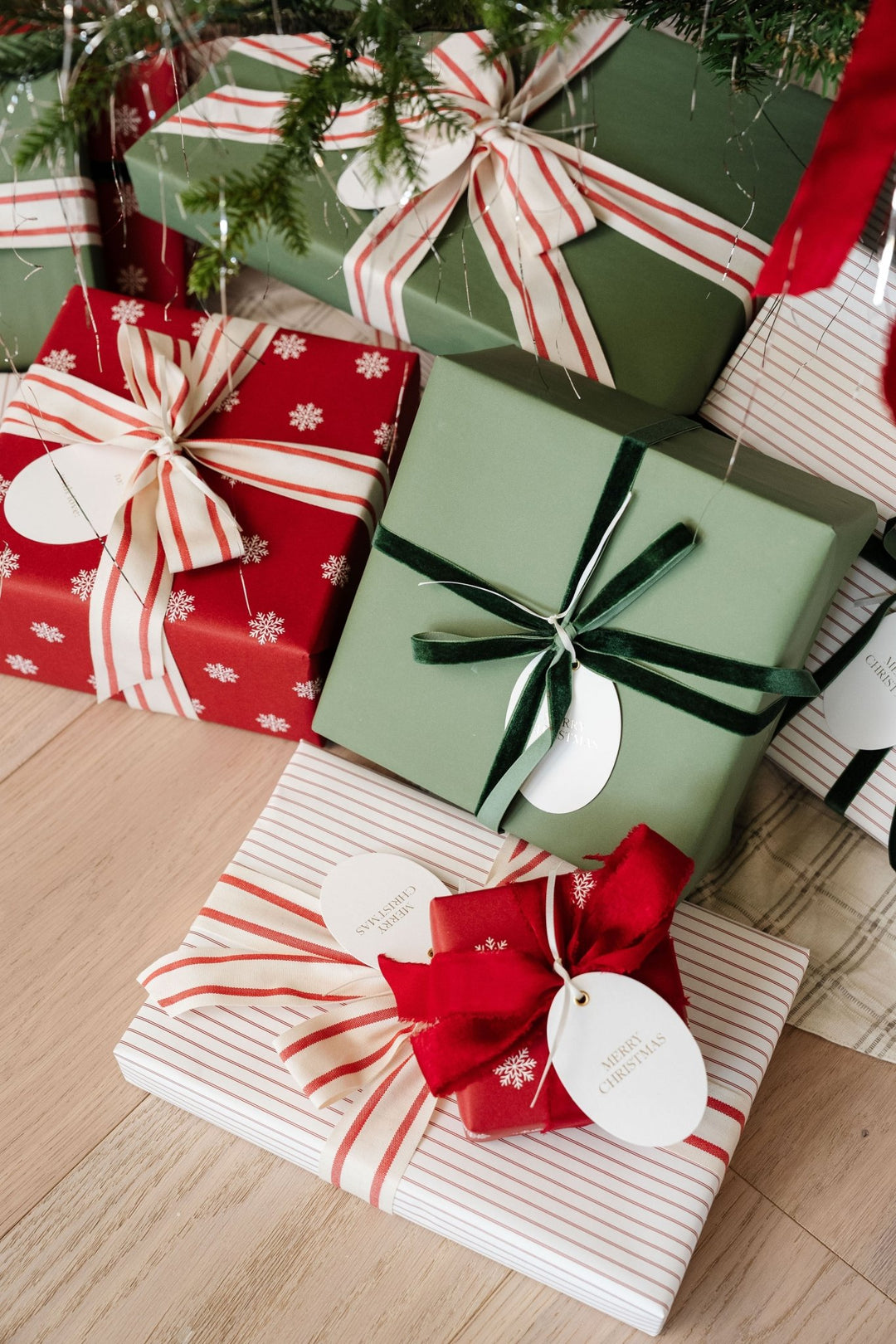 Red snowflake, pinstripe, and green presents with striped bows tucked under the Christmas tree