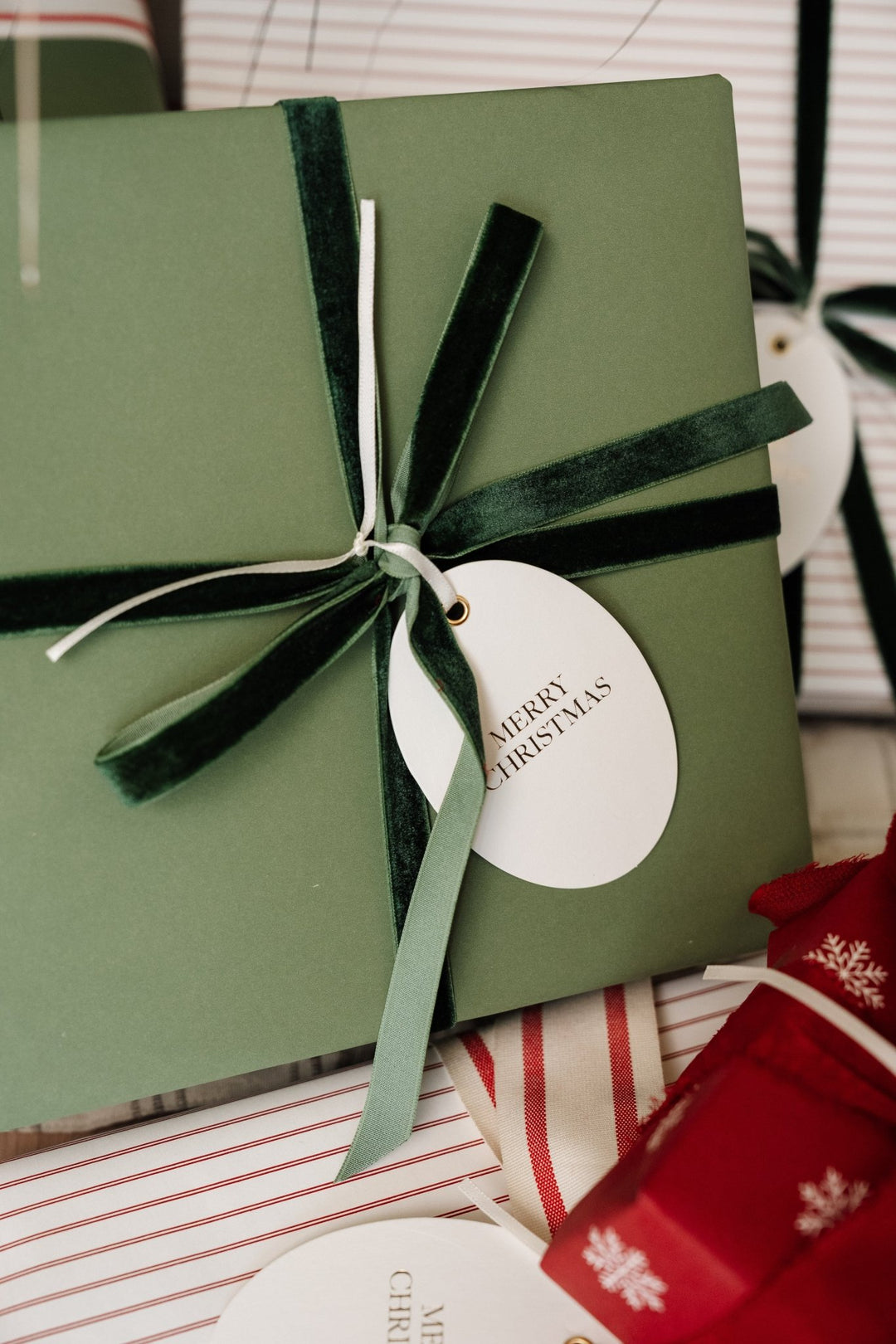 Soft green wrapped gift tied with deep green velvet ribbon and an oval Merry Christmas tag