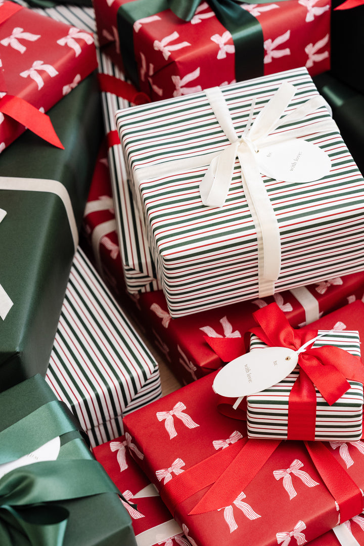 Close pile of Christmas presents in red bow, stripe, and green paper tied with red, green, and cream ribbons