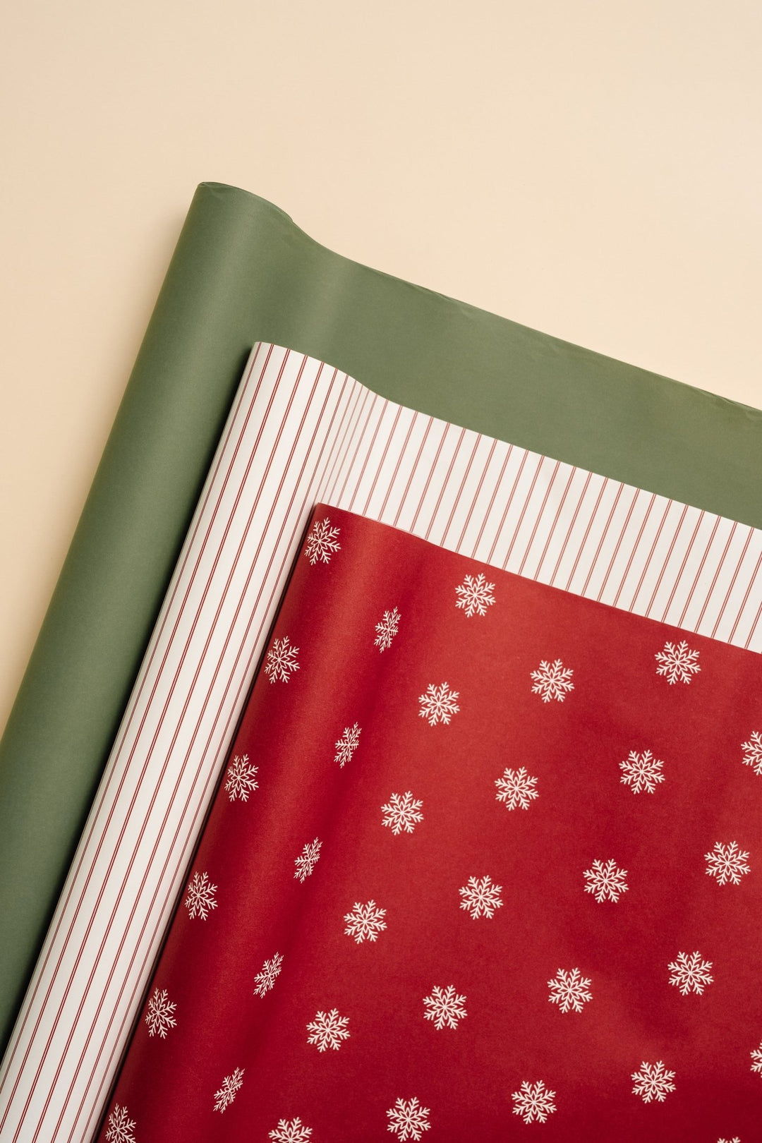 Sheets of soft green, cream pinstripe, and red snowflake wrapping paper layered on cream