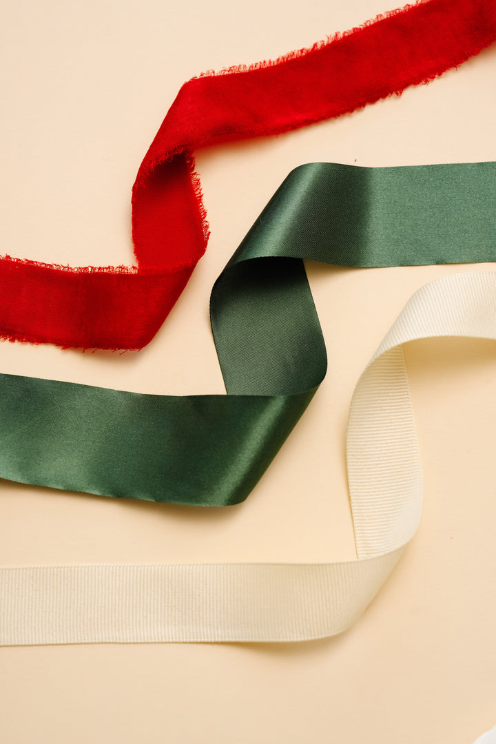 Frayed red velvet, green satin, and cream grosgrain ribbon lengths across a cream backdrop