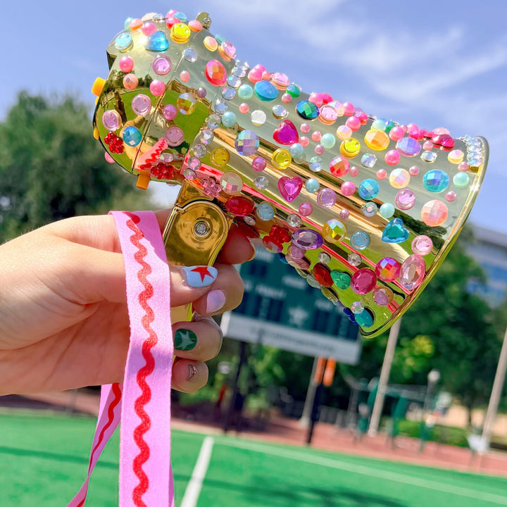 Gold megaphone decorated with colorful rhinestones held up on a sports field