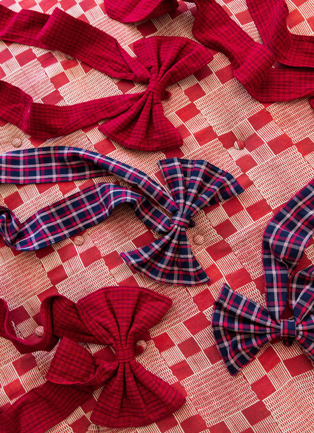Navy plaid and crimson red fabric bows arranged together on a pink patterned cloth