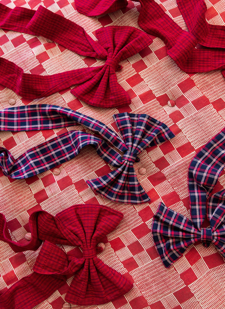 Navy plaid and crimson red fabric bows arranged together on a pink patterned cloth