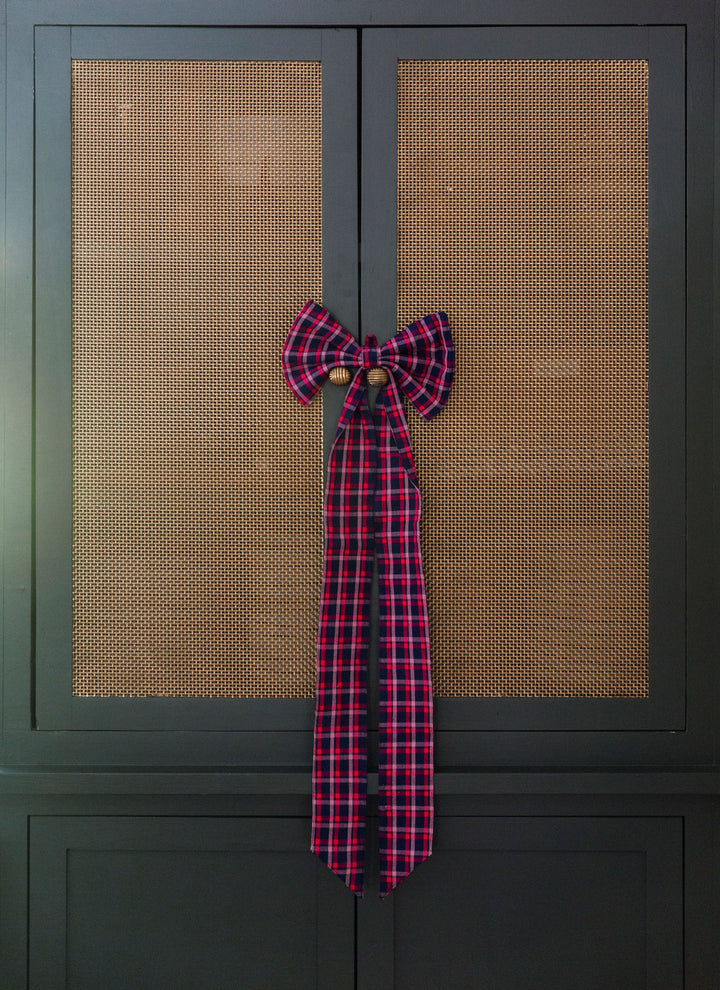Navy plaid fabric bow hung on a dark green cane door as holiday decoration