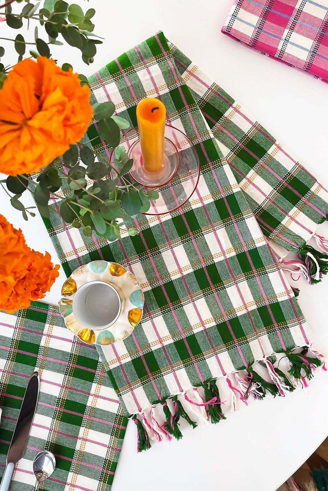 Green plaid kitchen towel on a table set with orange flowers, a candle, and gold candlesticks