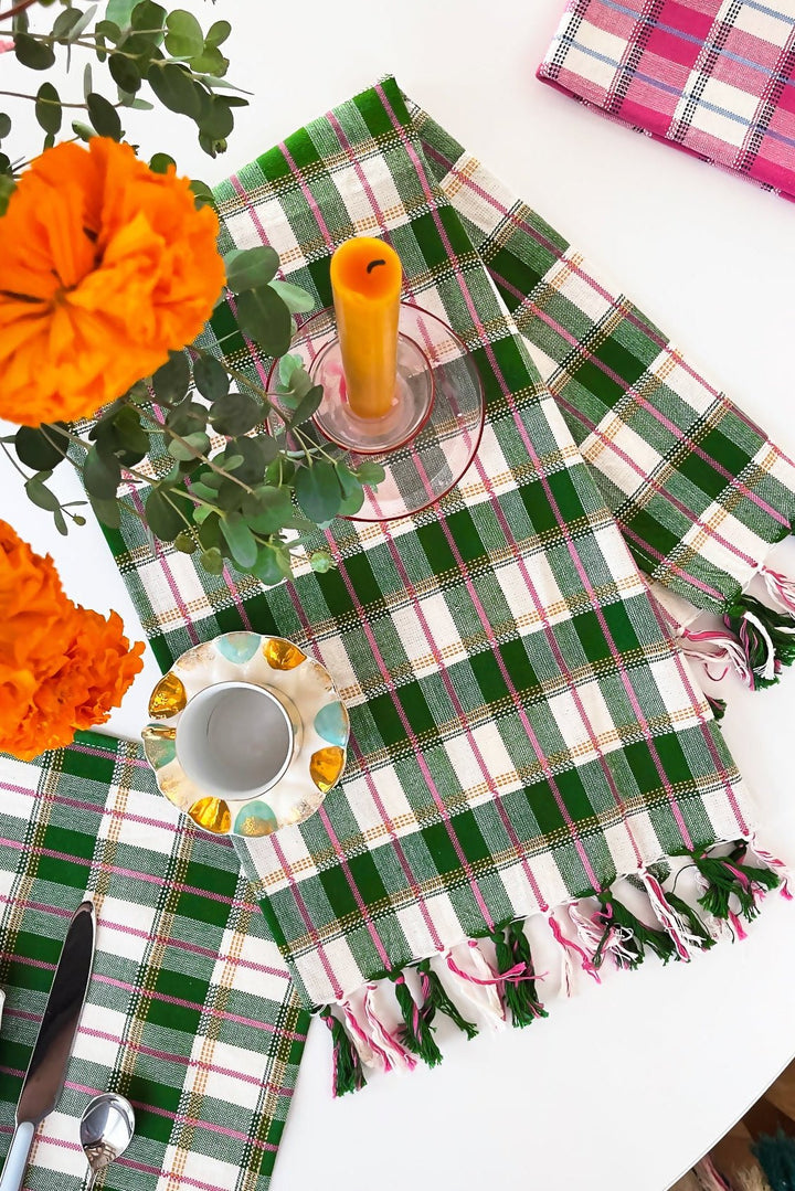 Green plaid kitchen towel on a table set with orange flowers, a candle, and gold candlesticks