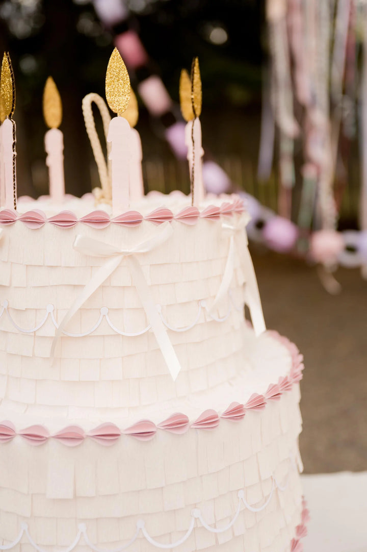 Close-up of a birthday cake pinata with lit candles and decorative ribbons.