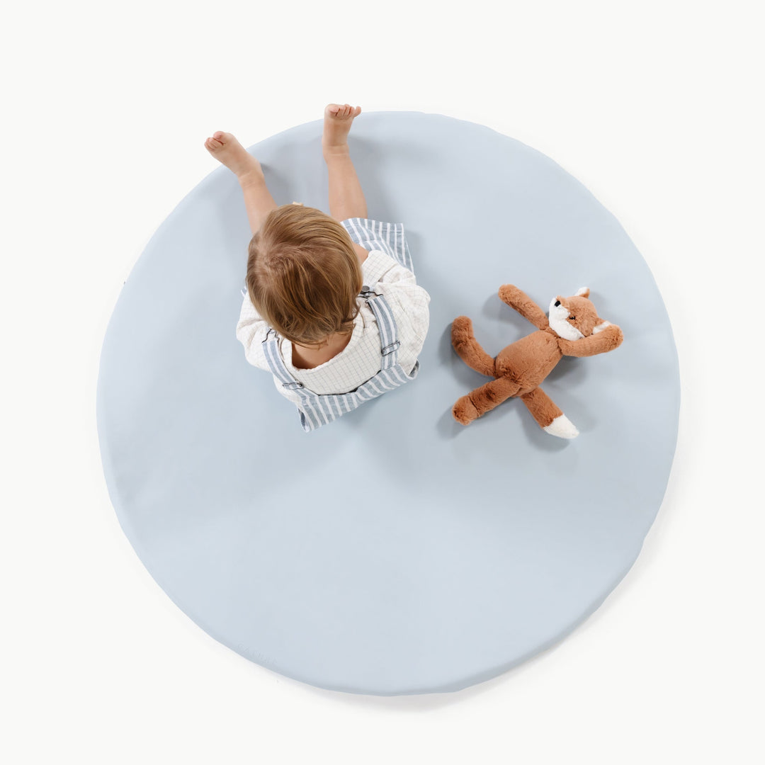 Light blue round padded baby play mat, overhead view with a toddler and plush fox.