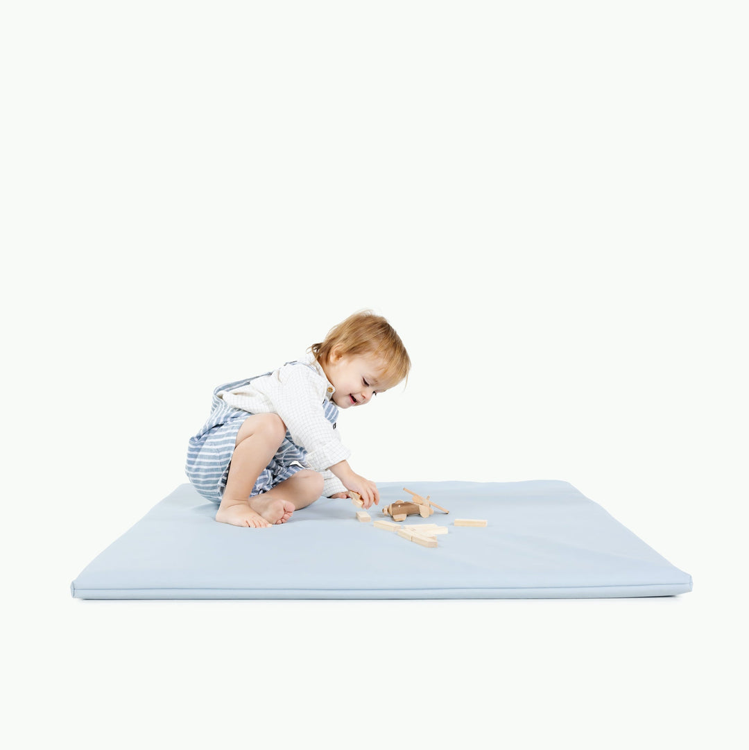 Light blue padded baby play mat with a toddler playing on it during tummy time.