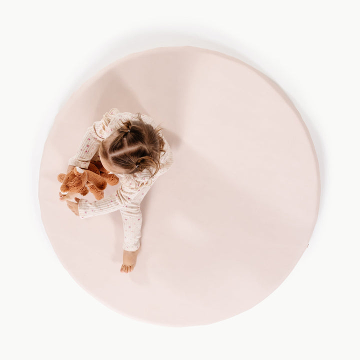 Cream blush round padded baby play mat, overhead view with a toddler and plush toy.