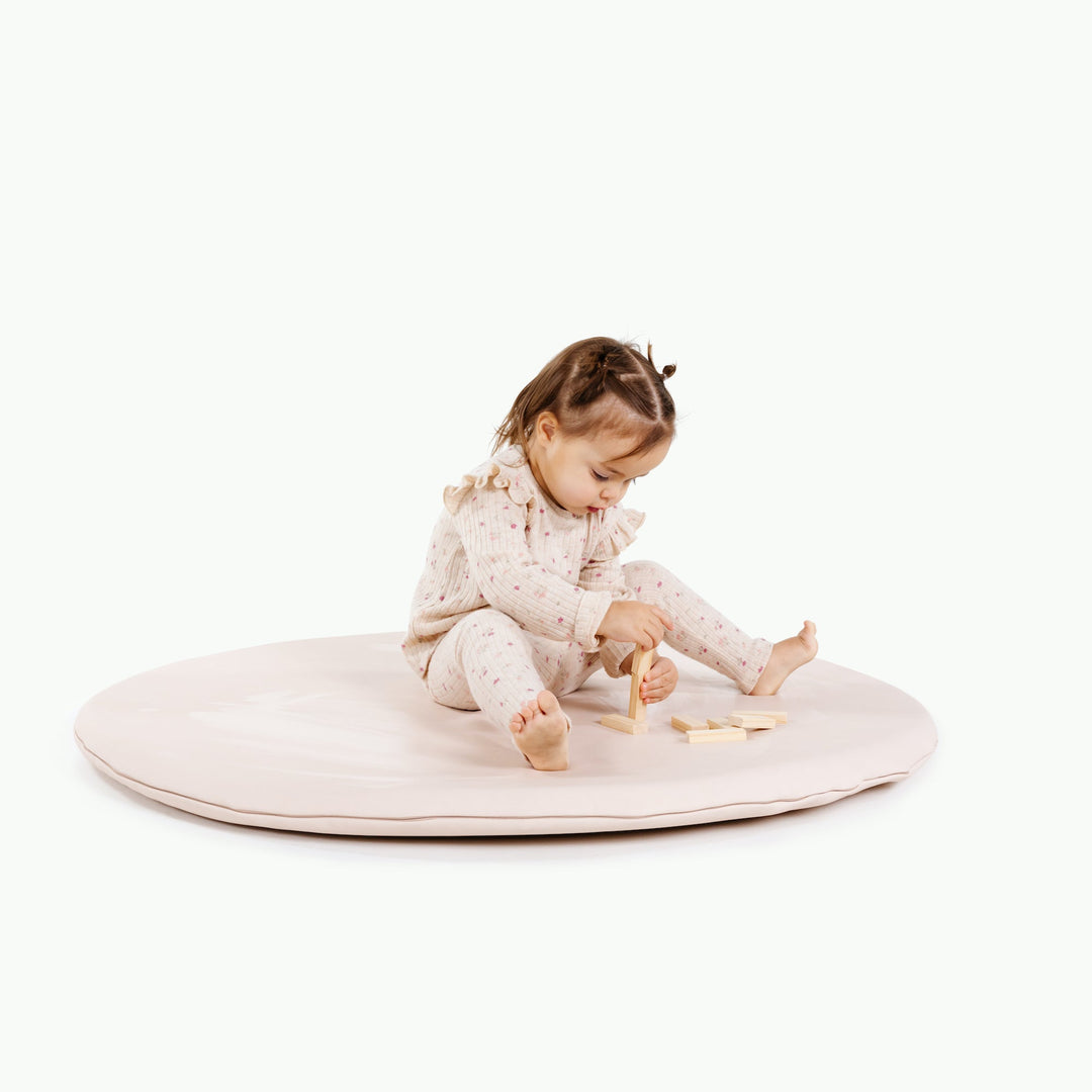 Cream blush round padded play mat with a toddler playing with wooden blocks.