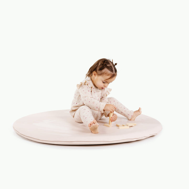 Cream blush round padded play mat with a toddler playing with wooden blocks.