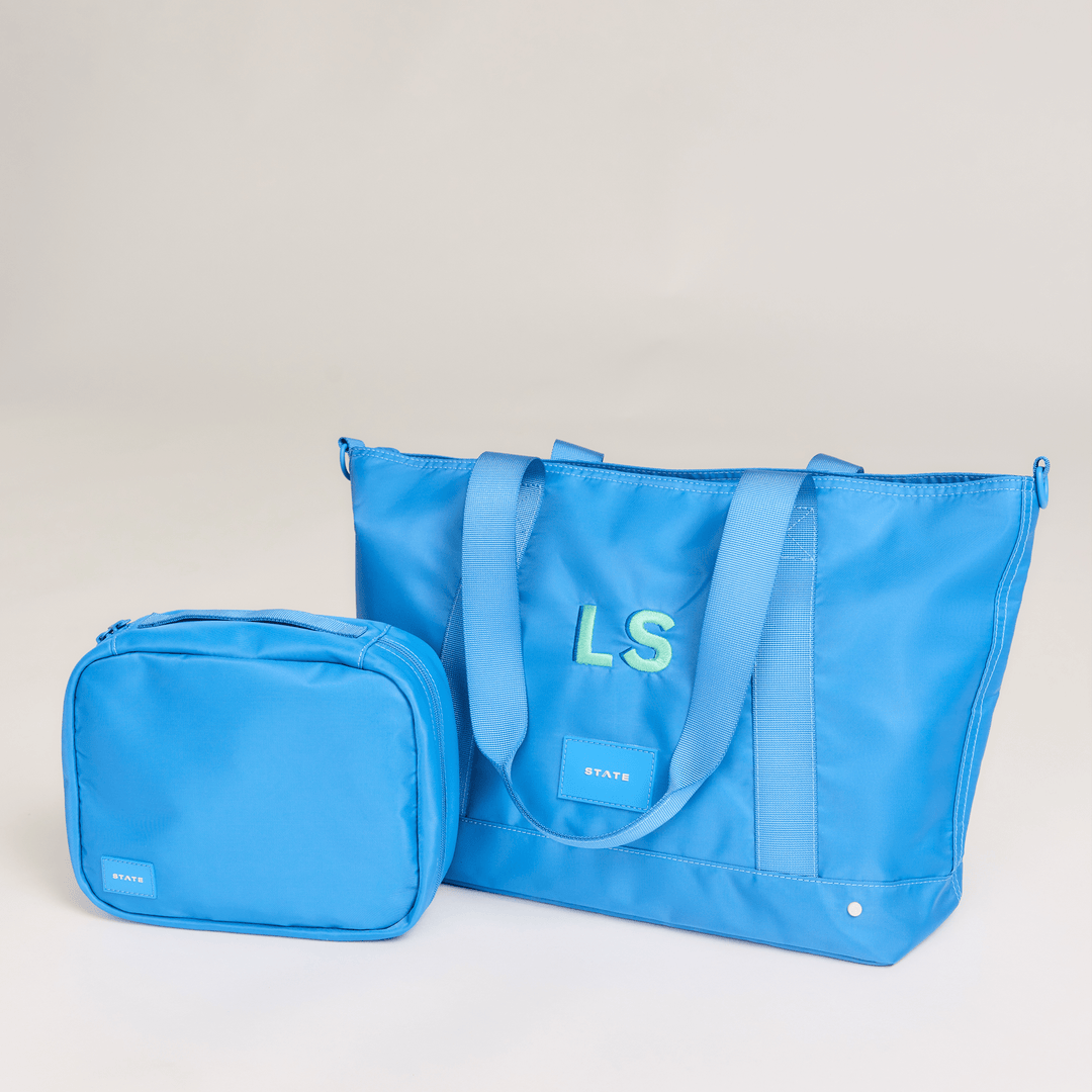 Blue Bensen toiletry bag in a lifestyle scene beside a matching blue STATE tote with a monogram