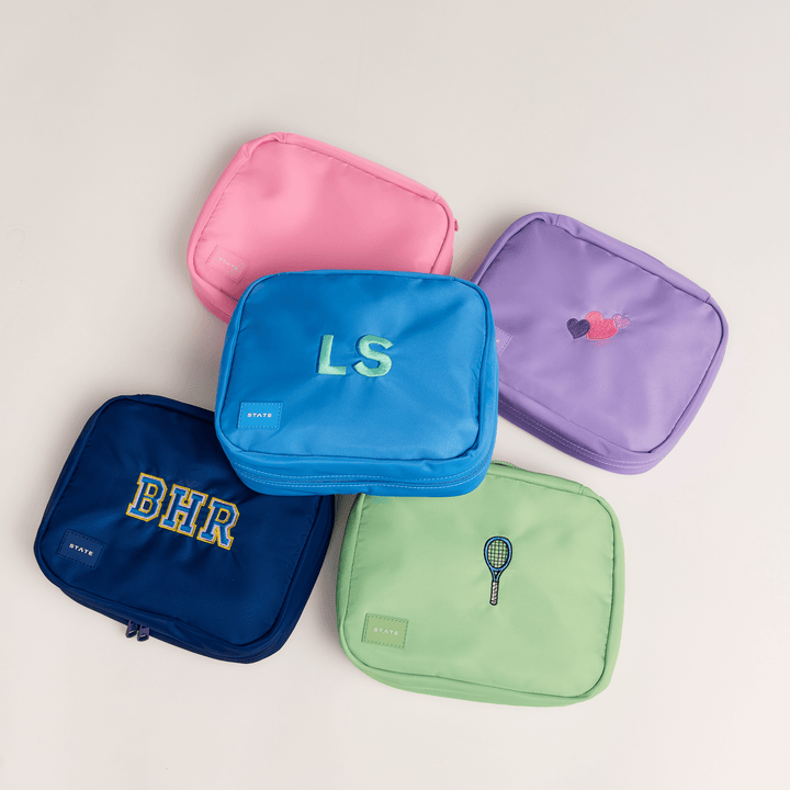 Overhead group of Bensen toiletry bags in pink, blue, lilac, green, and navy with monograms