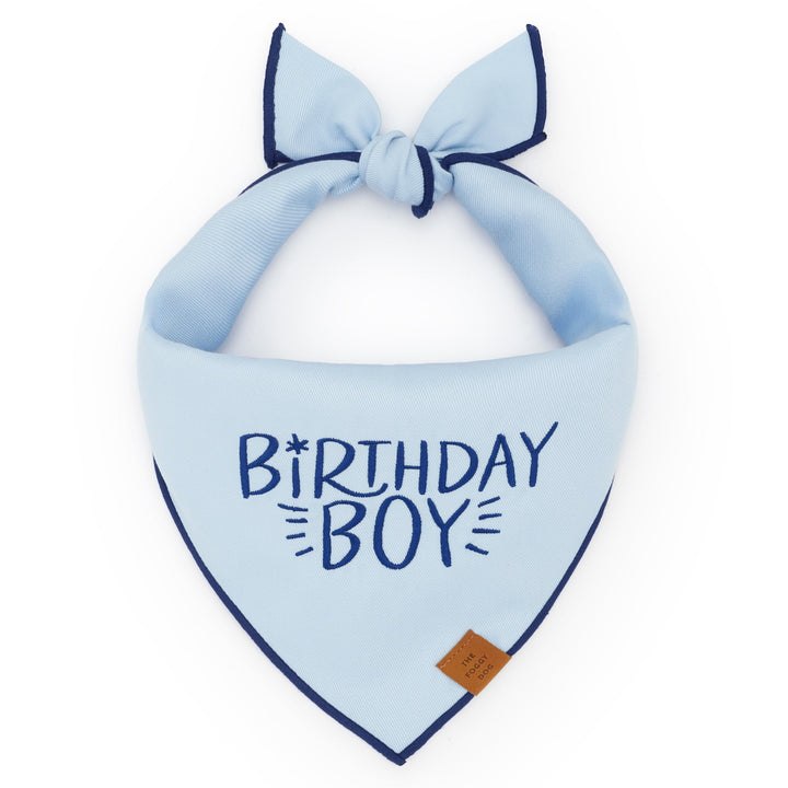 Light blue dog bandana embroidered Birthday Boy in navy, tied flat on white with a tan tag
