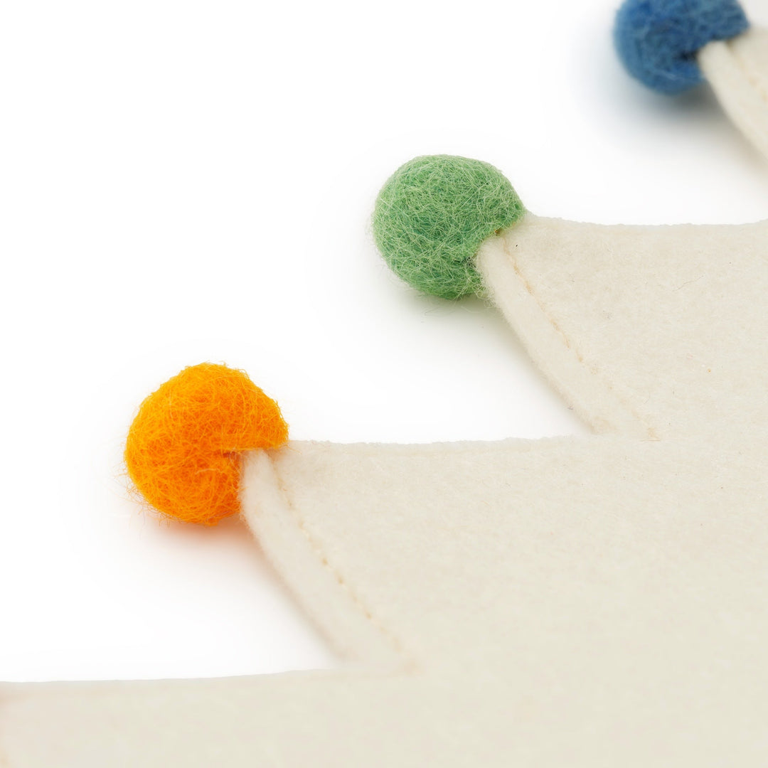 Close-up of the ivory felt crown points with orange, green, and blue wool pom-poms