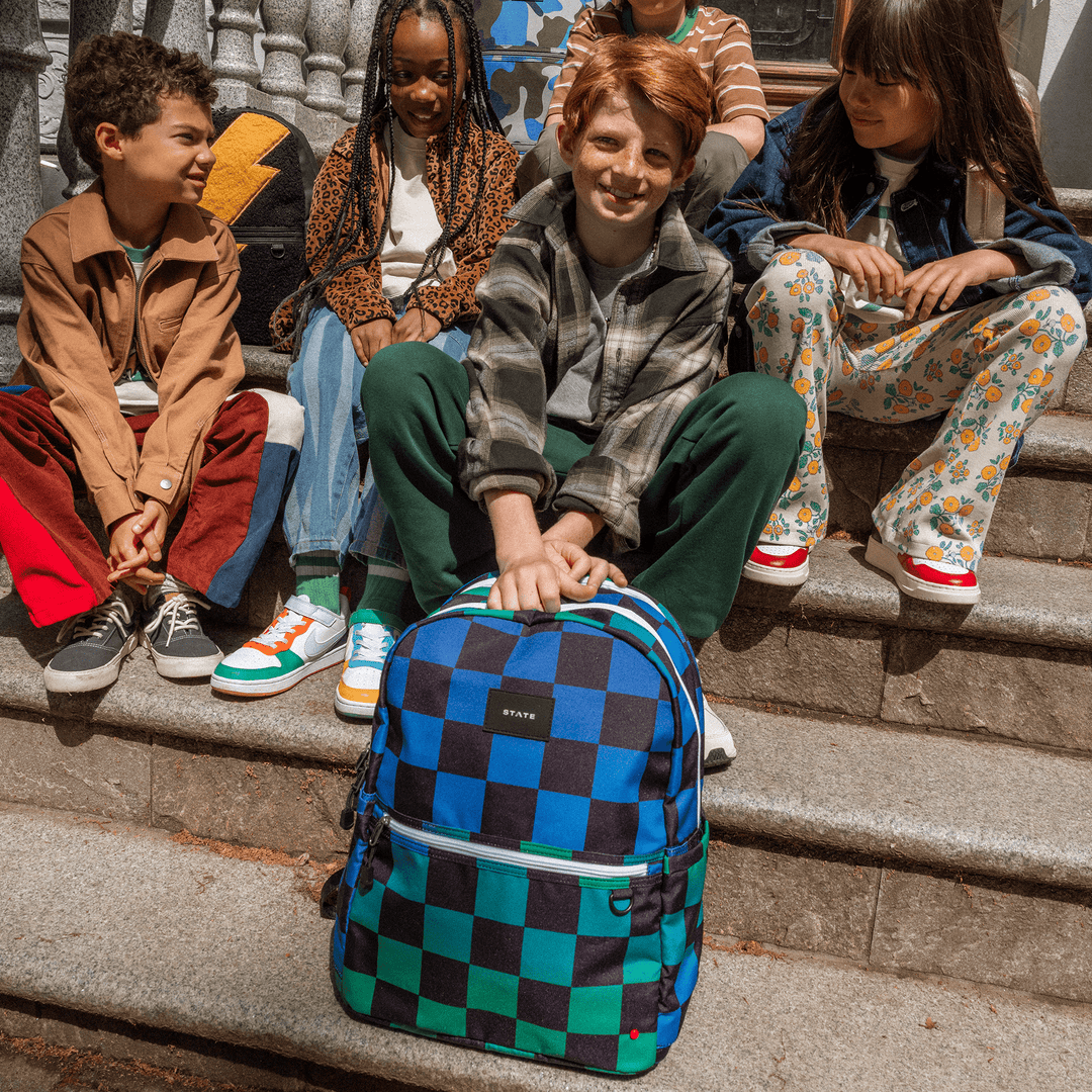 Group of kids on city steps, one with the Blue Checkerboard STATE Kane backpack