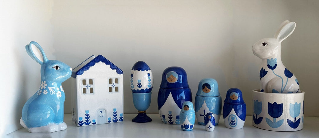 Blue tulip cup grouped with blue and white bunnies, a ceramic house, and blue nesting dolls on a shelf
