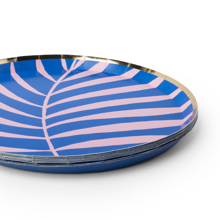 A stack of round paper plates featuring a blue and pink palm leaf pattern with a metallic gold rim, photographed on a clean white background.