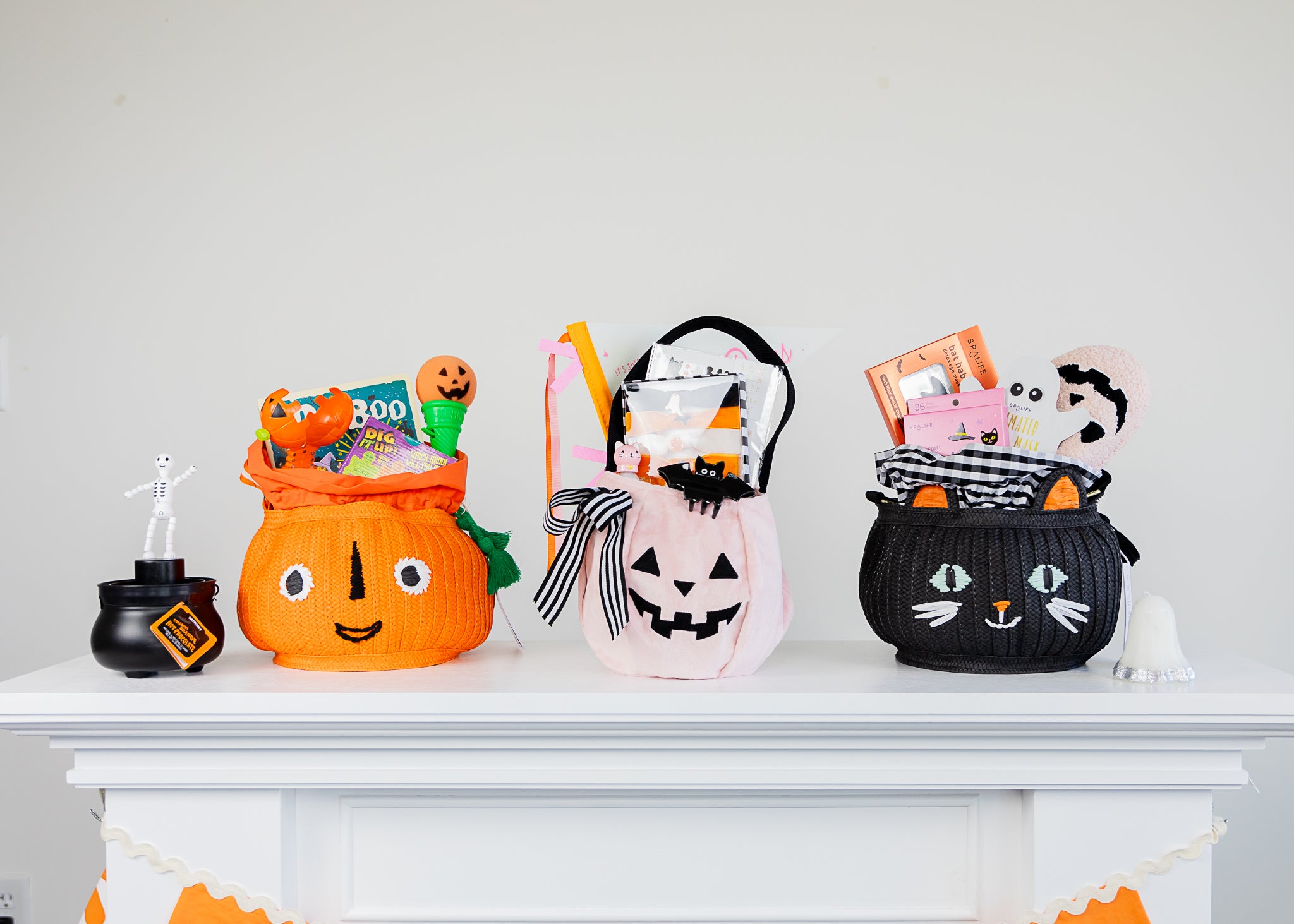A lineup of 3 boo baskets for kids and adults on a white mantle filled with Halloween toys