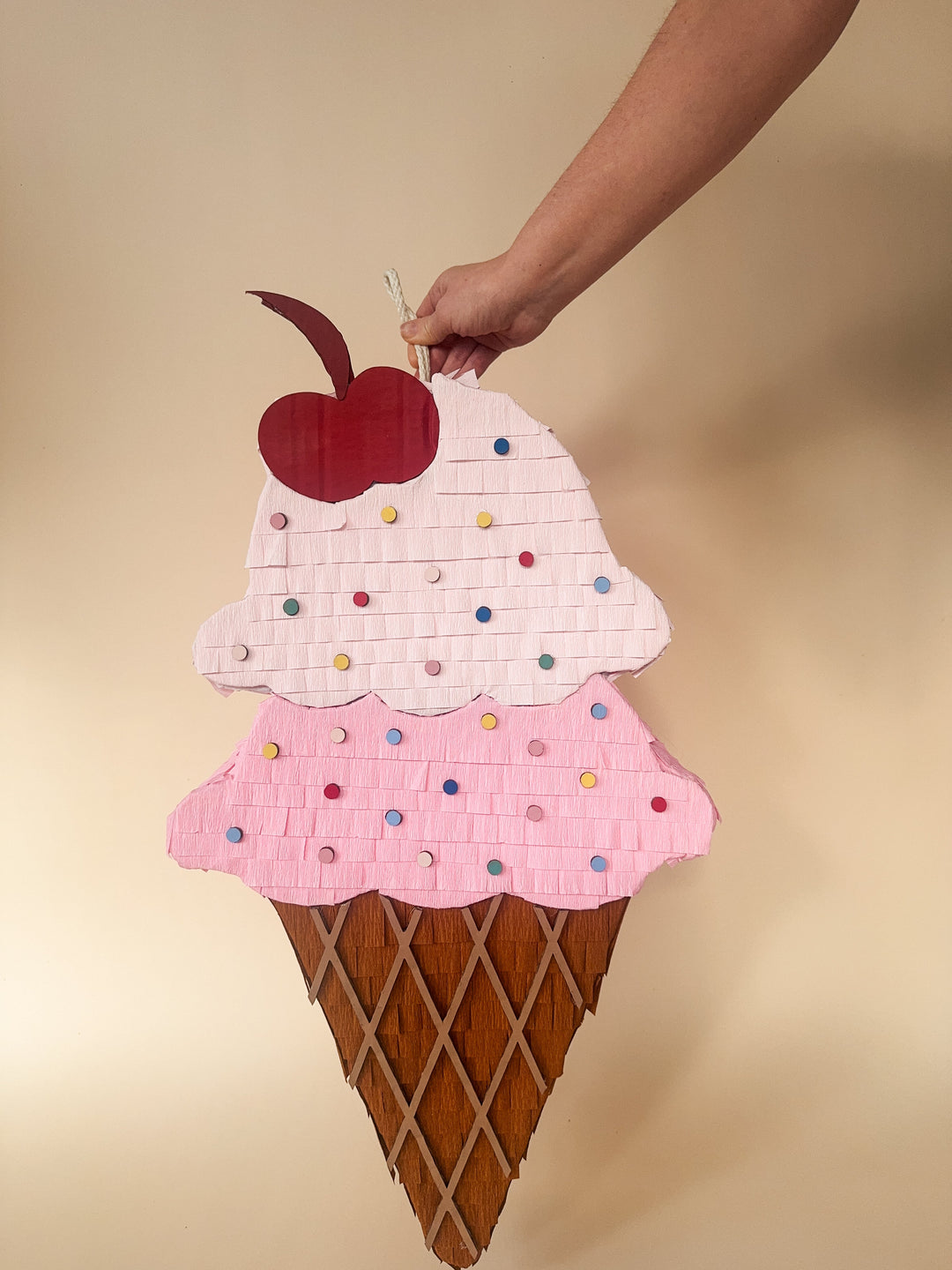 Handmade ice cream cone pinata with a cherry on top against a beige background