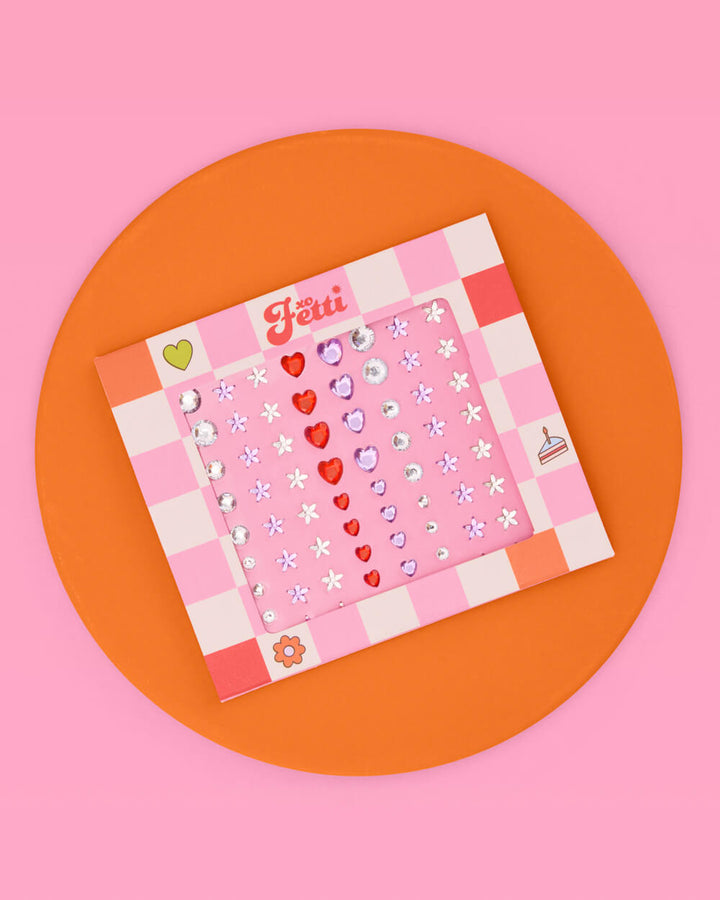 Heart and daisy eye gem card on an orange circle against a pink background