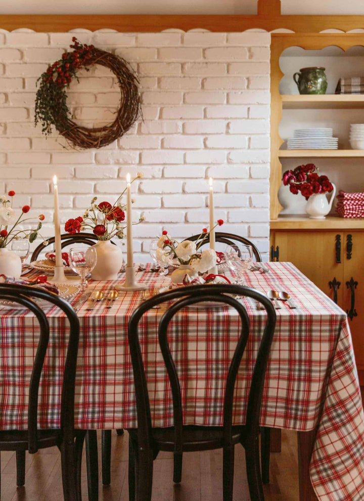 Clara plaid tablecloth draped over a table edge, red and blue plaid on cream with tassels