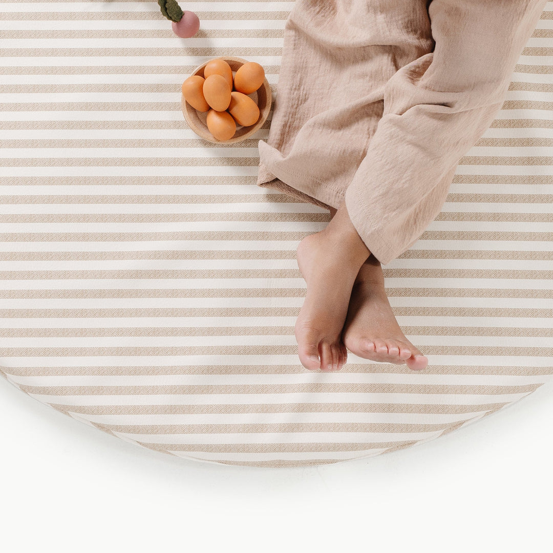Overhead view of a child on the cafe stripe padded play mat with a bowl of wooden play food