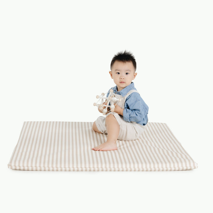 Boy sitting on the square cafe stripe padded play mat holding a wooden ball toy