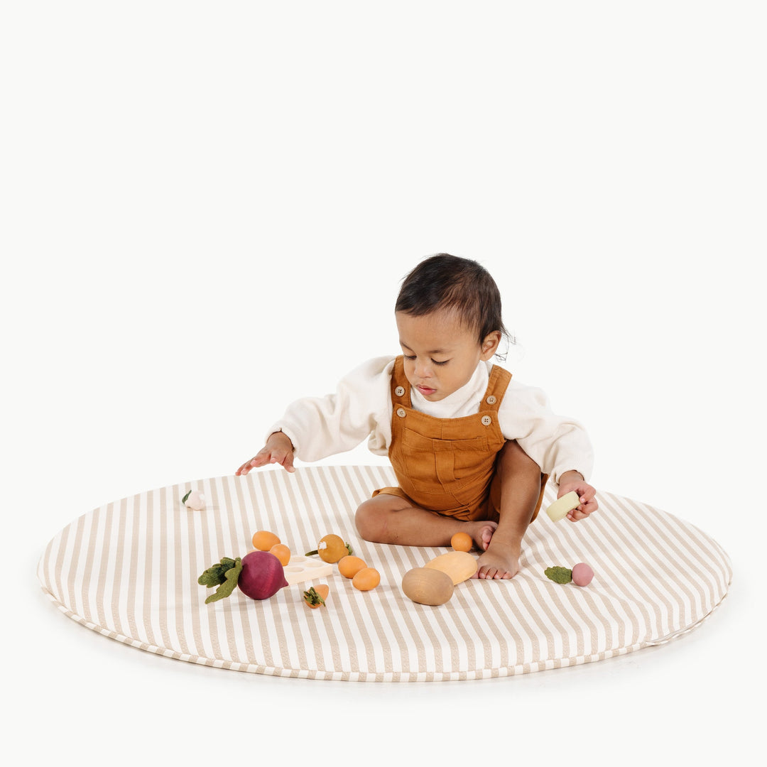 Toddler sitting on the round cafe stripe padded play mat with wooden play vegetables