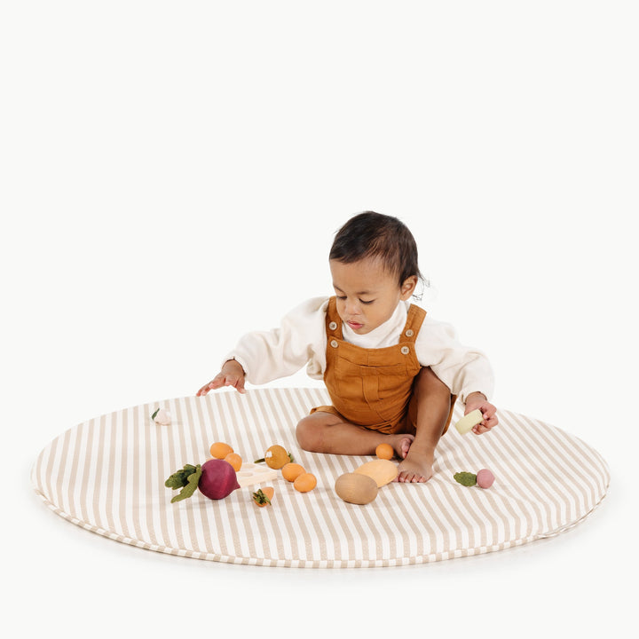 Toddler sitting on the round cafe stripe padded play mat with wooden play vegetables