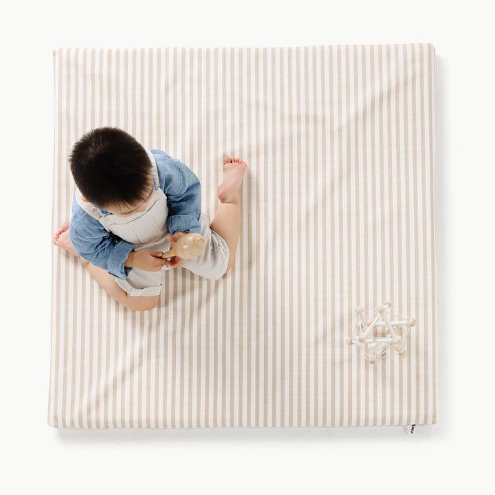 Overhead view of a child playing on the square cafe stripe padded play mat with a wooden ball toy