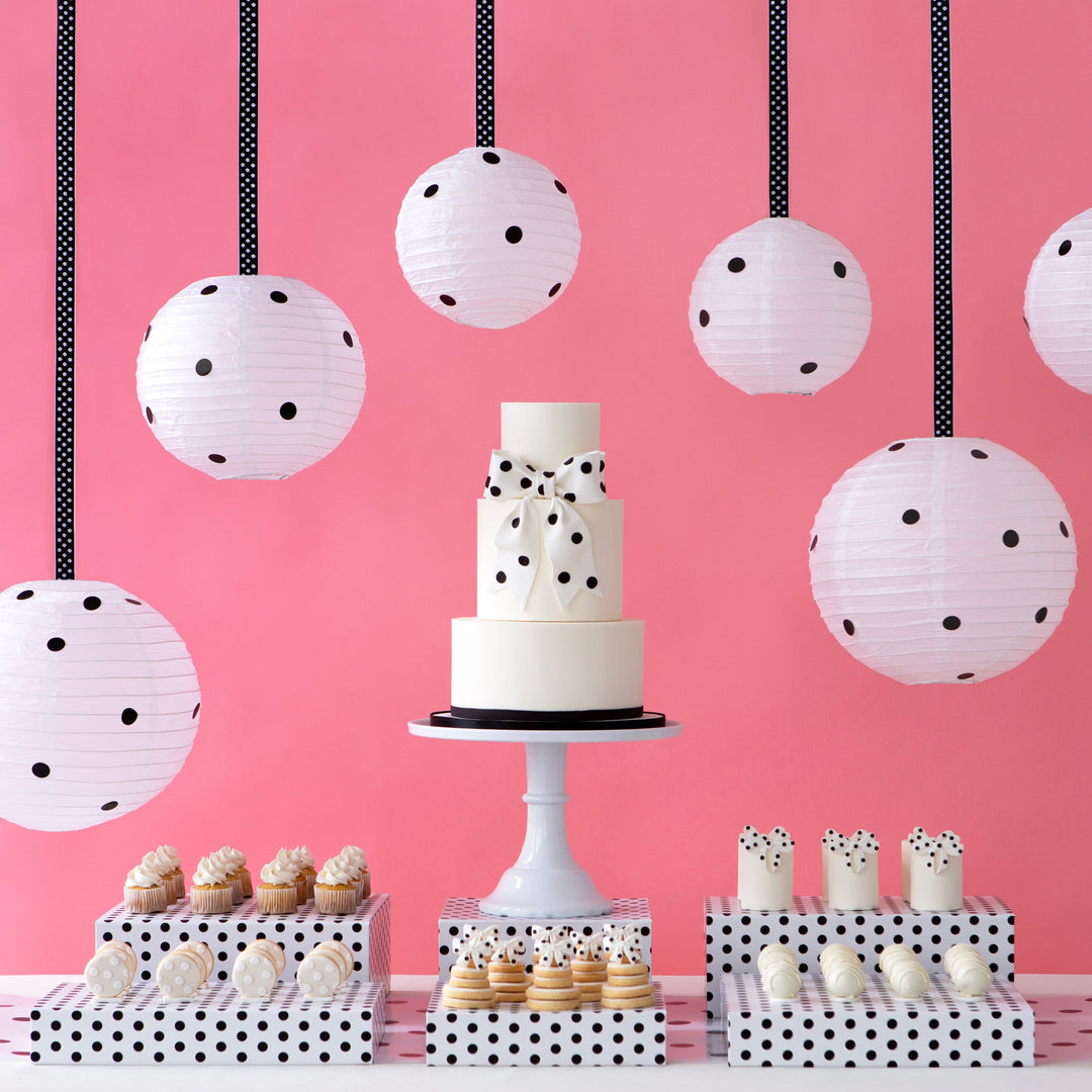 Decorative dessert table with polka dot paper lanterns against a pink wall.