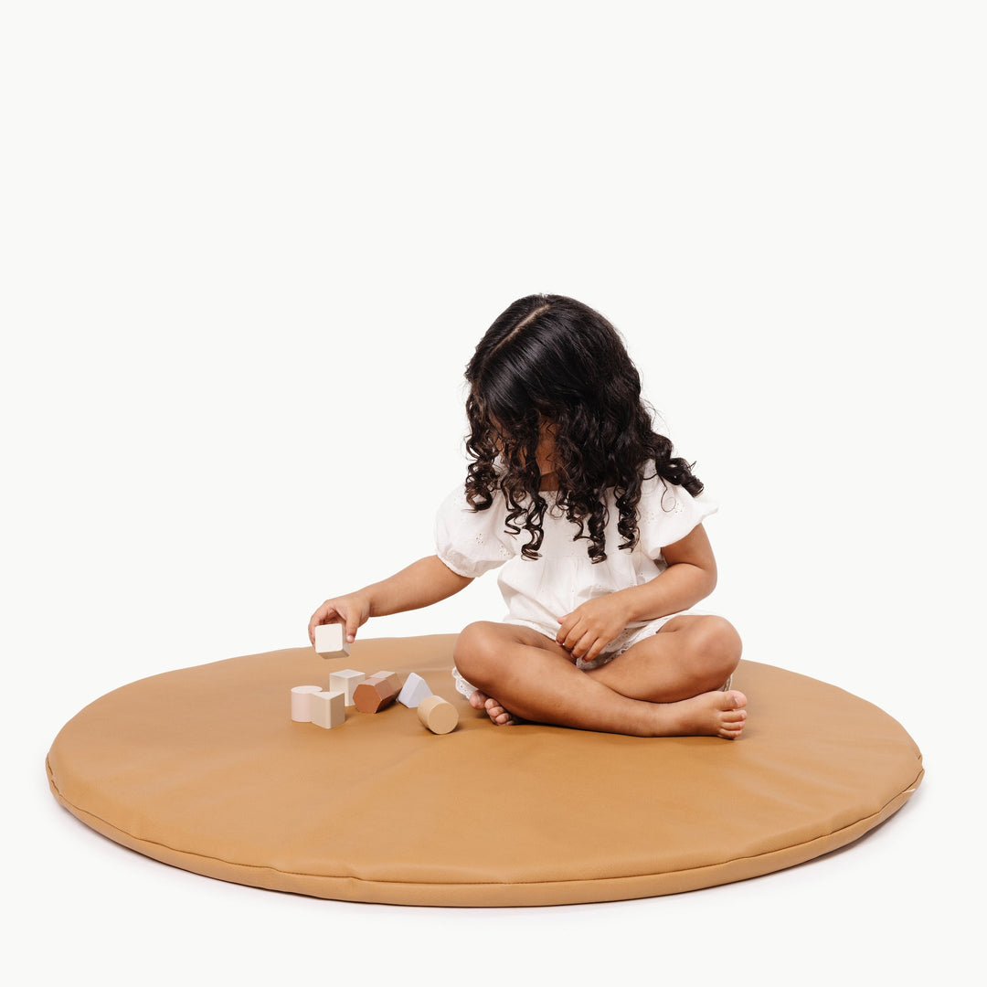 Girl sitting on the round camel vegan leather padded play mat stacking wooden blocks