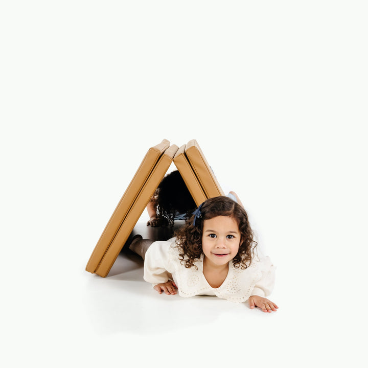 Two children peeking out from under the camel tumbling mat propped into a tent