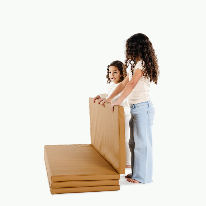 Two girls unfolding the camel vegan leather folding tumbling mat for active indoor play