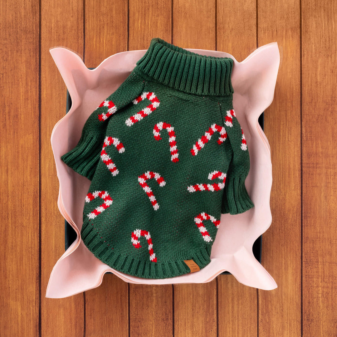 Green candy cane sweater folded in pink tissue inside a wooden gift crate