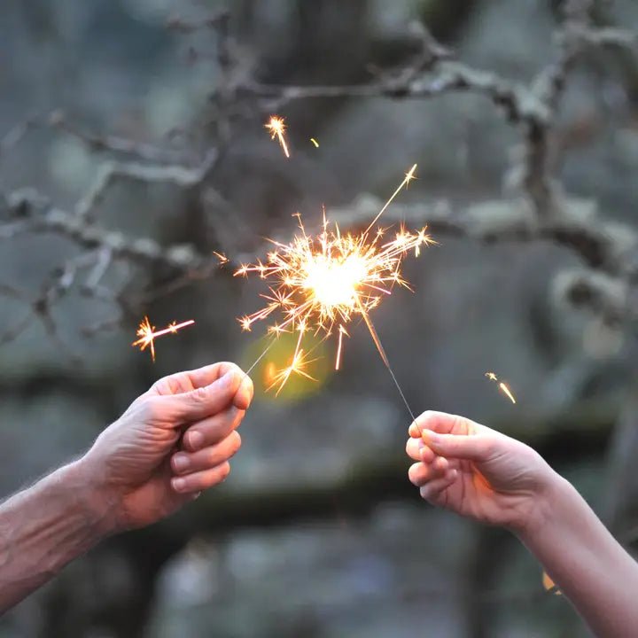 Two hands holding lit gold sparklers glowing against a dark background for a celebration