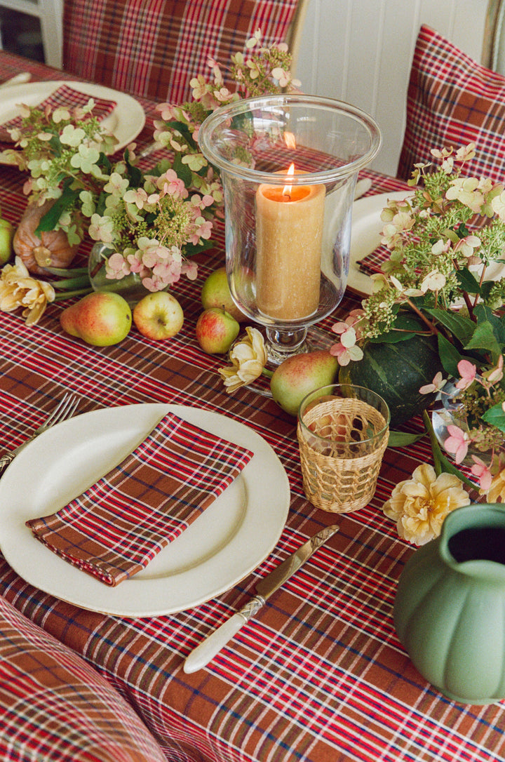 Charlotte plaid tablecloth on a long table with hurricane candles, apples, and blossom branches