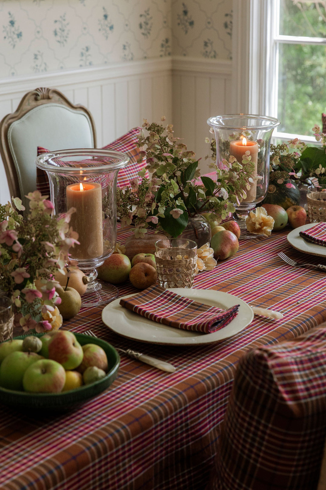 Charlotte plaid tablecloth set for a holiday dinner with green apples, candles, and dried hydrangea