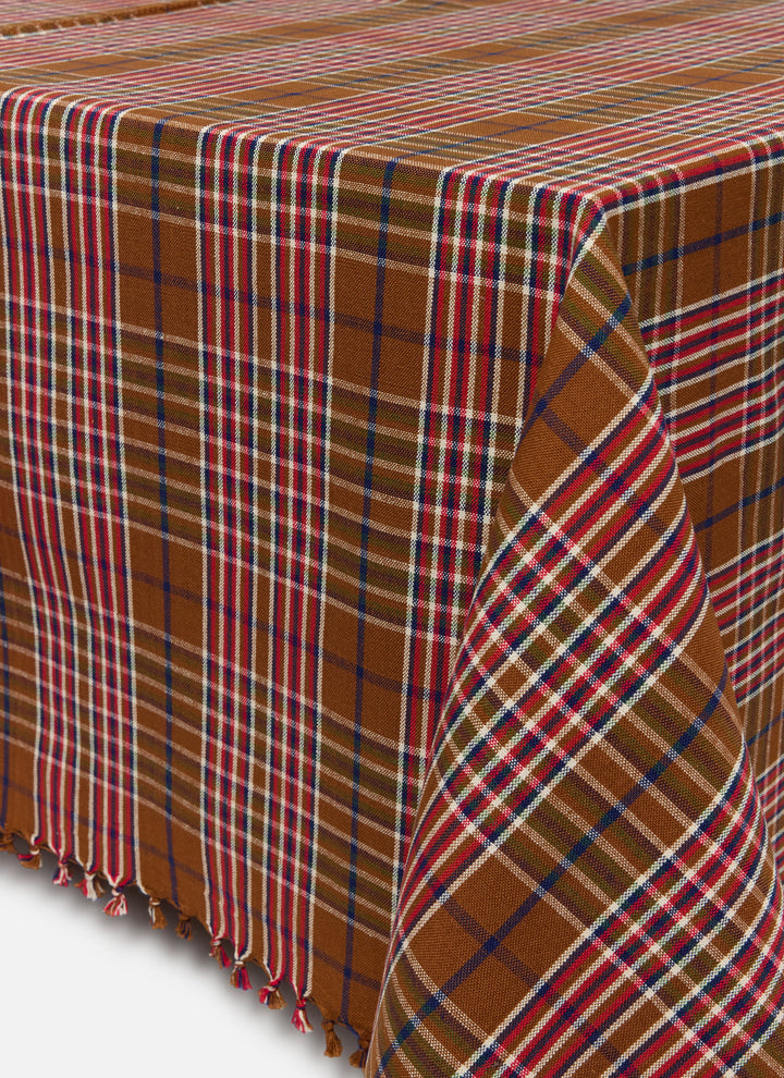 Charlotte plaid tablecloth in nutmeg, red, indigo, and olive draped to show its tasseled edge